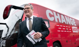 Keir Starmer smiles as he holds a copy of the Labour manifesto next to his election battlebus.