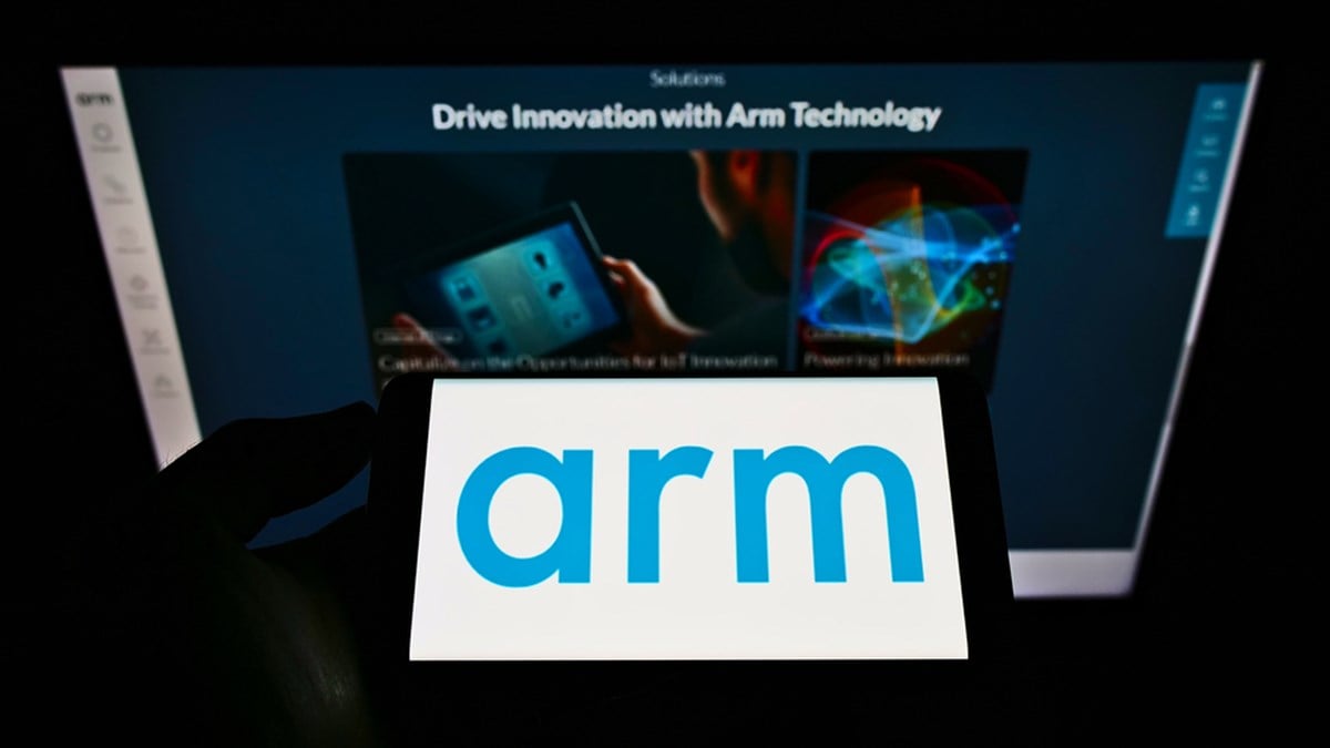Person holding mobile phone with logo of British semiconductor company Arm Ltd. on screen in front of business webpage.