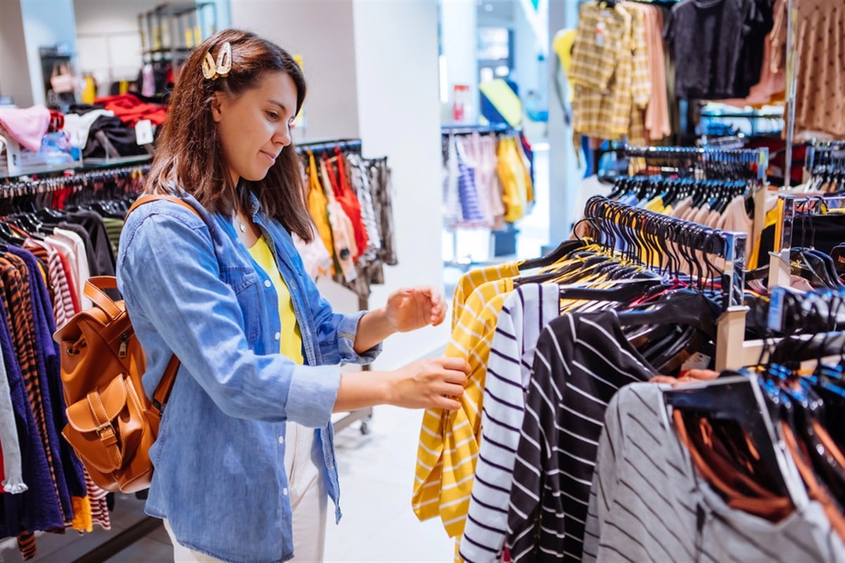Woman in clothes store looking at shirts on hangers — Photo