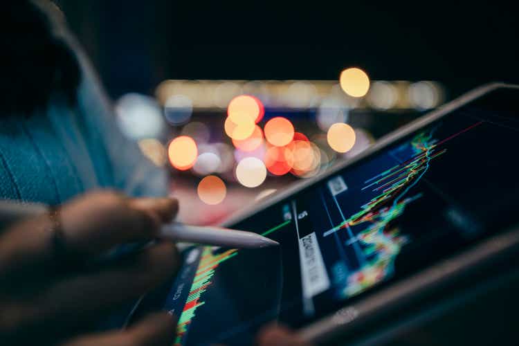 Close-up of female hands holding a mobile phone, browsing the stock market charts on a city street at night, with blurred car and street lights in the background