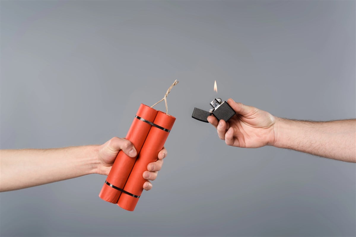 Cropped view of men holding dynamite and lighter on grey background