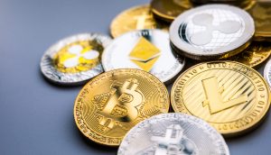 Eine Sammlung verschiedener physischer Münzen, darunter Bitcoin, Ethereum, Ripple und Litecoin, die verschiedene Kryptowährungen auf einer grauen Oberfläche darstellen.