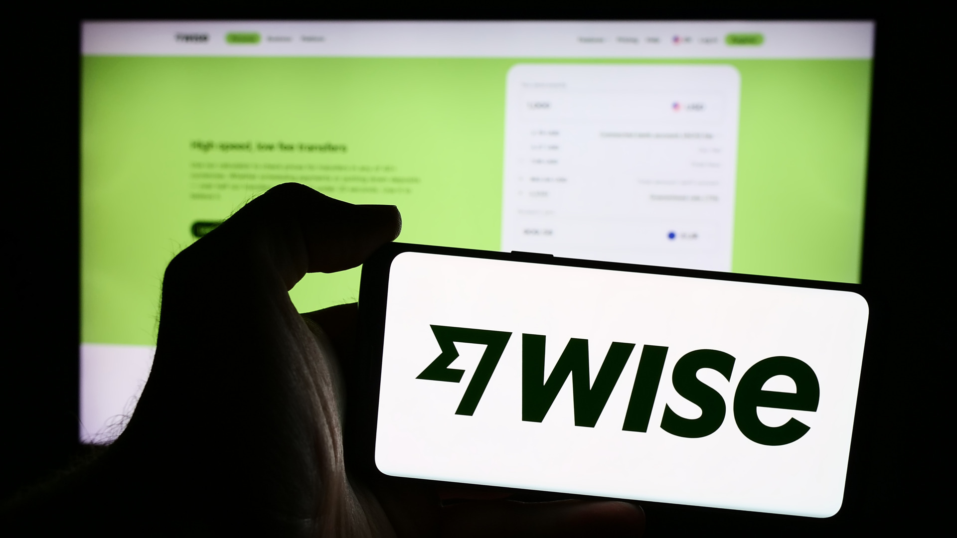 Person holding mobile phone with logo of British financial technology company Wise plc in front of business web page. Focus on phone display.