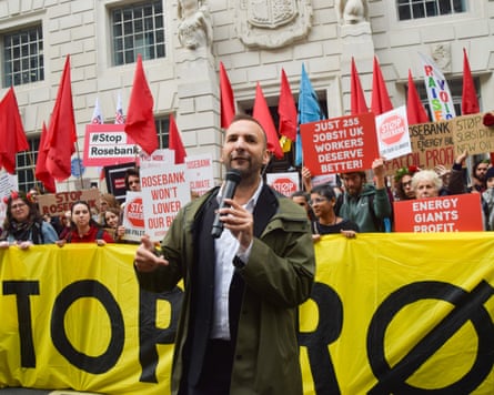 Zack Polanski stands in front of protesters at a rally holding a microphone