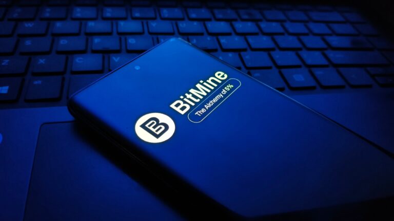 Closeup of a dark blue smartphone displaying the bitmine logo and text, resting on a laptop keyboard in a dimly lit, bluetoned environment , New York City, 15 December 2025