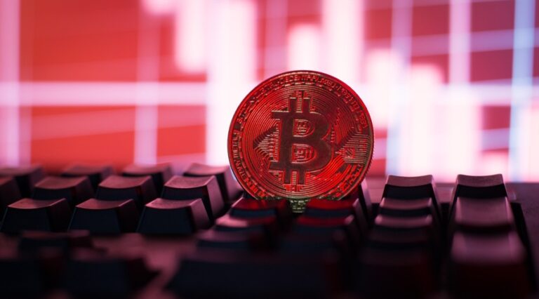 Bitcoin token standing on a PC keyboard with reddish light and red background
