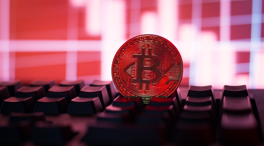 Bitcoin token standing on a PC keyboard with reddish light and red background