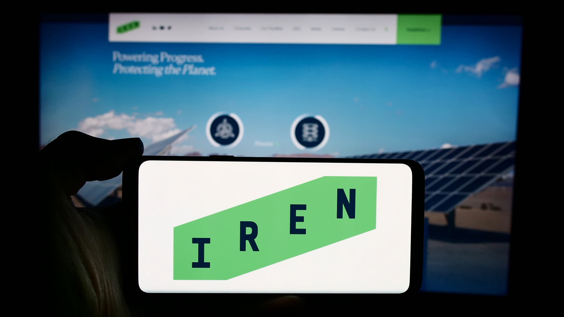Person holding cellphone with logo of Australian Bitcoin mining company Iris Energy Ltd. (IREN) in front of webpage. Focus on phone display.