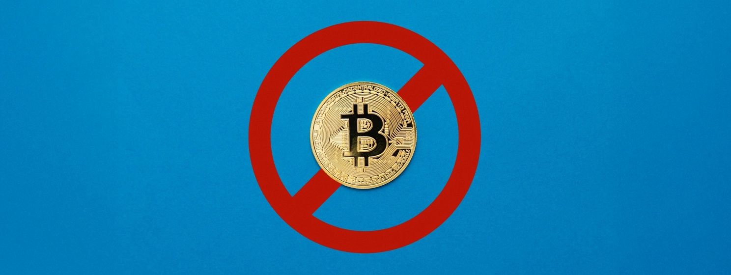 A physical Bitcoin coin centered within a red prohibition sign on a blue background.