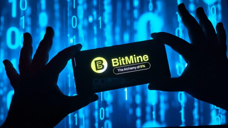 Silhouetted hands holding smartphone with BitMine logo on screen