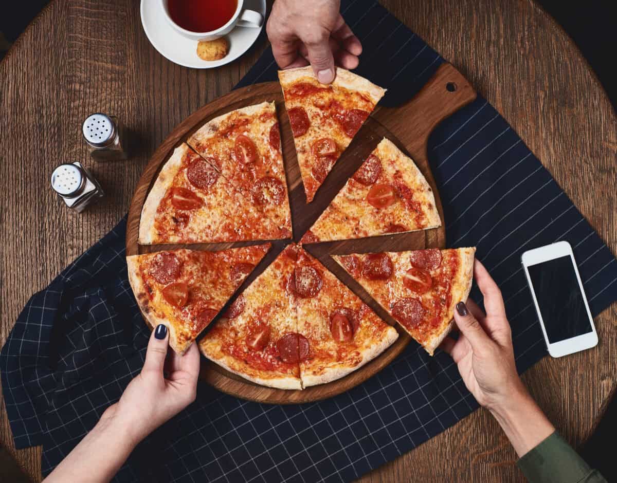 Close-up of people hands taking slices of pepperoni pizza from wooden board.