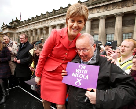 Nicola Sturgeon with her arm around then-husband Peter Murrell posing for the cameras as they cast their vote in the Scottish parliamentary election with a crowd of supporters behind them.